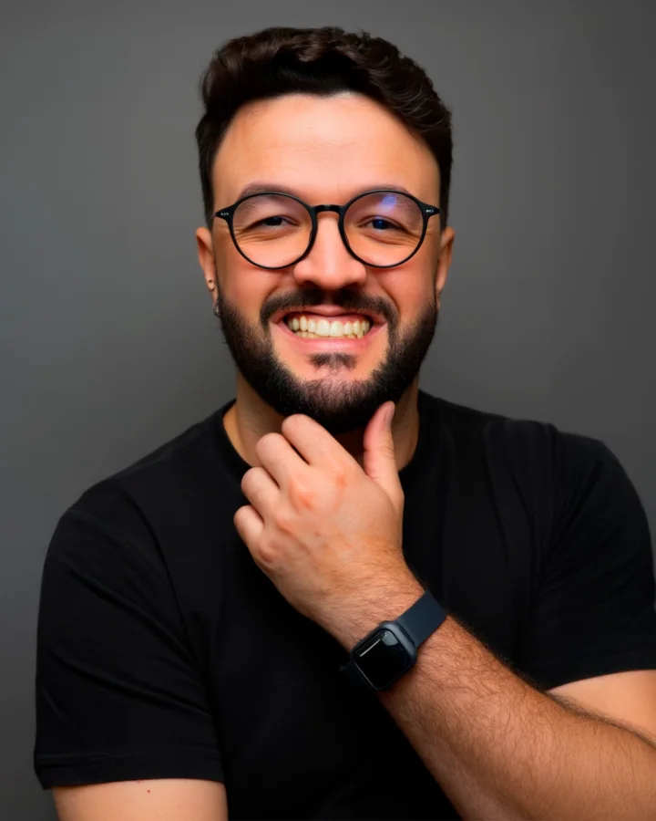 Jonatã Paixão, fundador da Contew, sorrindo para a câmera com a mão no queixo, de camiseta preta, óculos de armação redonda e relógio, sobre fundo cinza-escuro