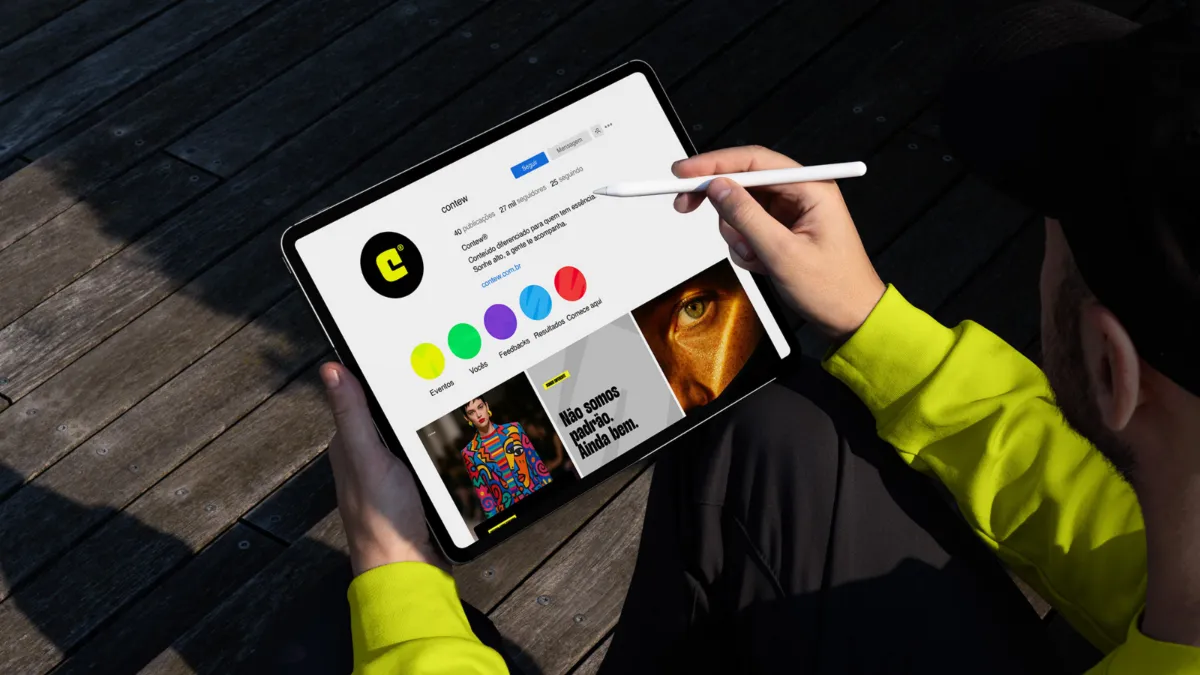 Pessoa de blusa amarela segurando um tablet com o perfil do Instagram da Contew aberto, mostrando a paleta de cores e posts da marca